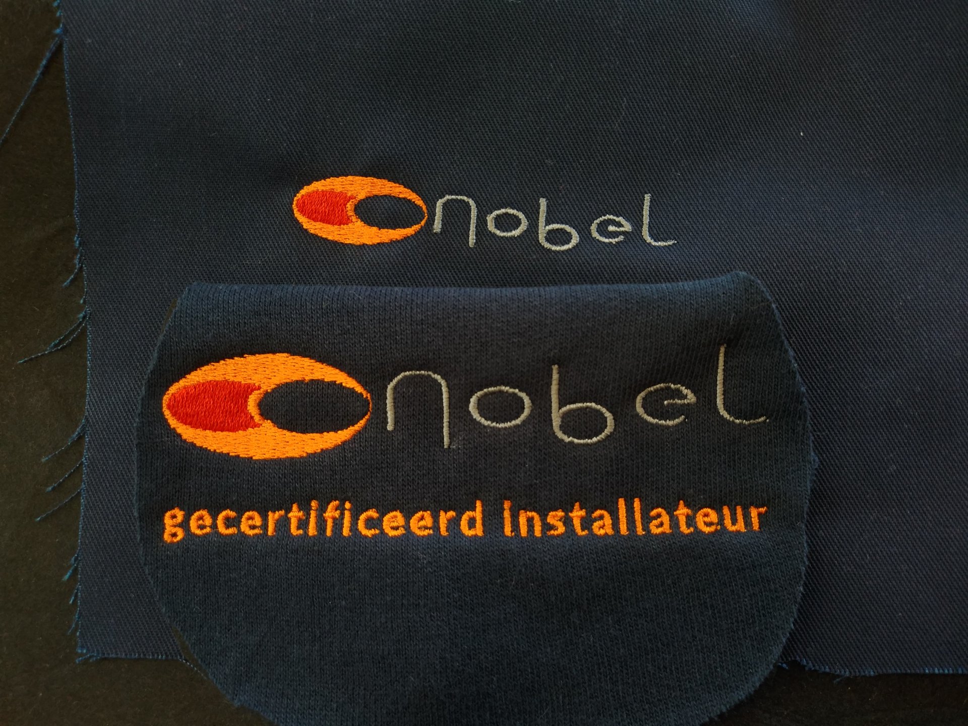 De bedrijfsnaam met beeldmerk Nobel geborduurd op kleding als voorbeeld